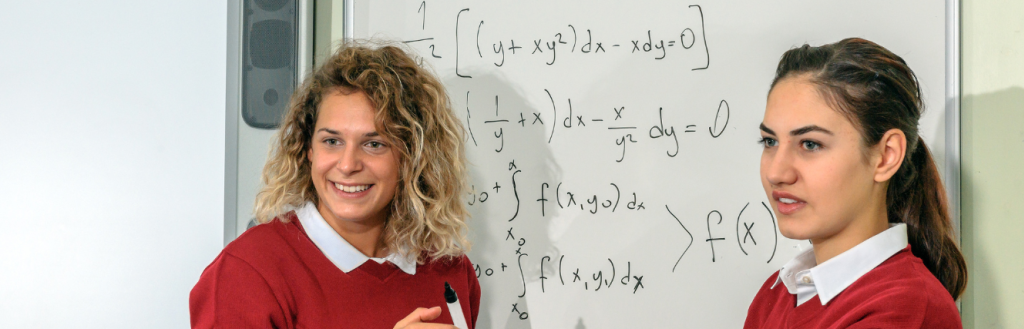 Two secondary school pupils stand by whiteboard with maths equations written on it