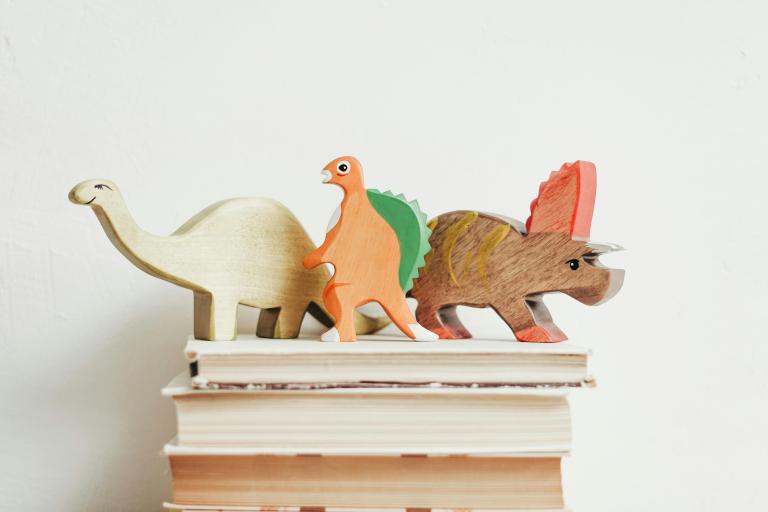 Three wooden dinosaurs on a stack of books