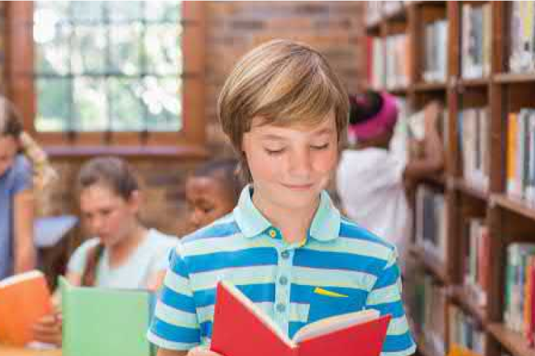Child standing in a library looking at a book
