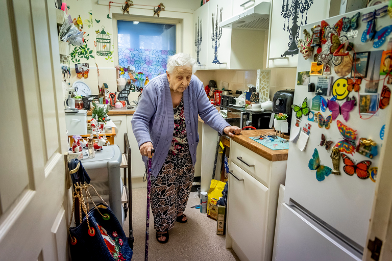 A lady walking in her kitchen using a walking stick