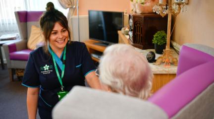 Smiling female carer with older lady sat in arm chair