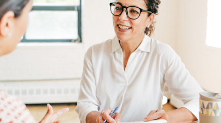 Two people talking at desk.