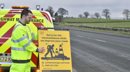 Highways worker holding a sign saying 'Sorry for the inconvenience while we improve your roads'