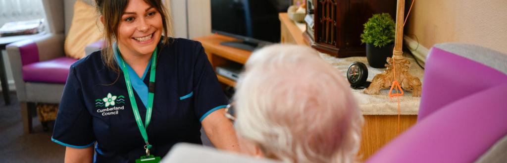 Smiling female carer with older lady sat in arm chair