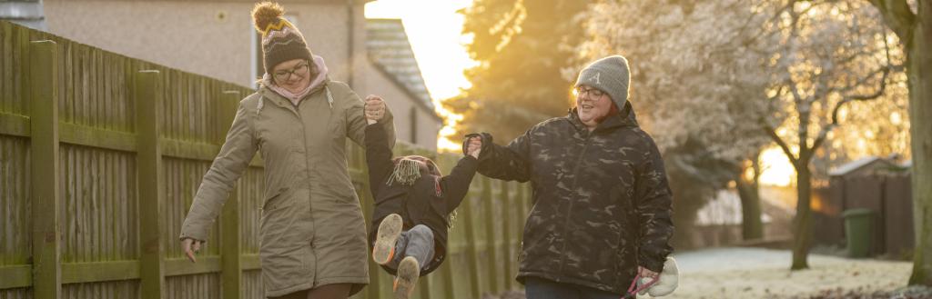 Two women outside swinging their young son between their arms