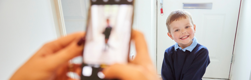 Young boy in school uniform stands in front of door for photograph, taken by out of focus mobile phone