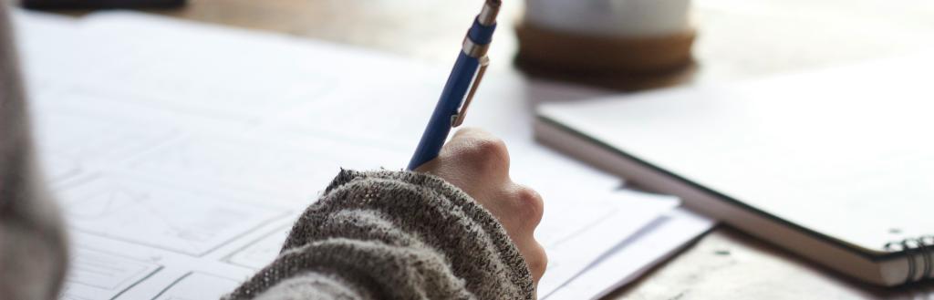 Close up of someone studying at a desk, with a cup of coffee.