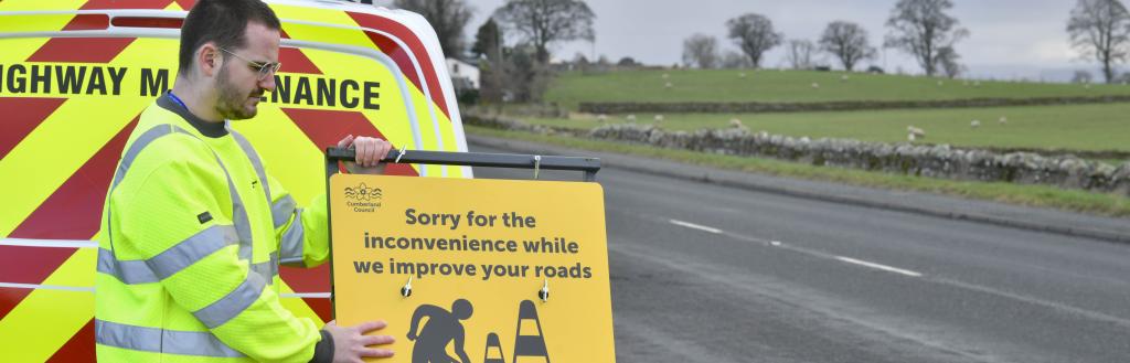 Highways worker holding a sign saying 'Sorry for the inconvenience while we improve your roads'
