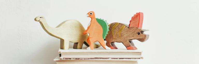 Three wooden dinosaurs on a stack of books