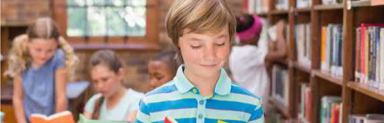 Child standing in a library looking at a book