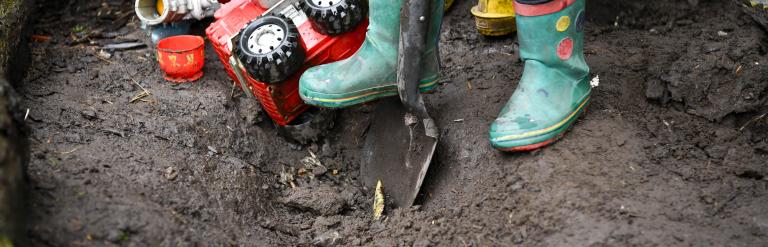 Child in wellington boots digging soil with a spade