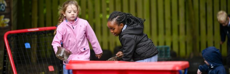 Two girls playing in a sand tray outside